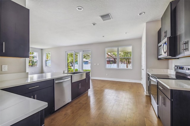 kitchen with wood-type flooring, appliances with stainless steel finishes, a textured ceiling, and sink