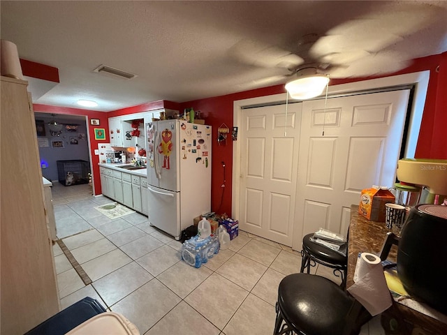 kitchen featuring a textured ceiling, ceiling fan, sink, white fridge, and light tile patterned flooring