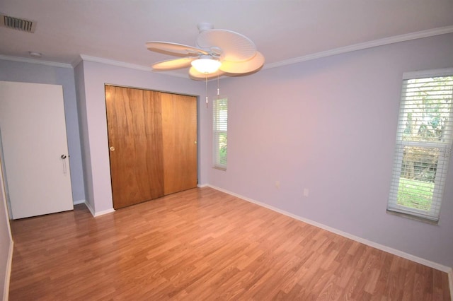 unfurnished bedroom with ceiling fan, a closet, crown molding, and light wood-type flooring