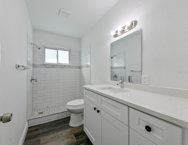 bathroom featuring vanity, toilet, a tile shower, and wood-type flooring