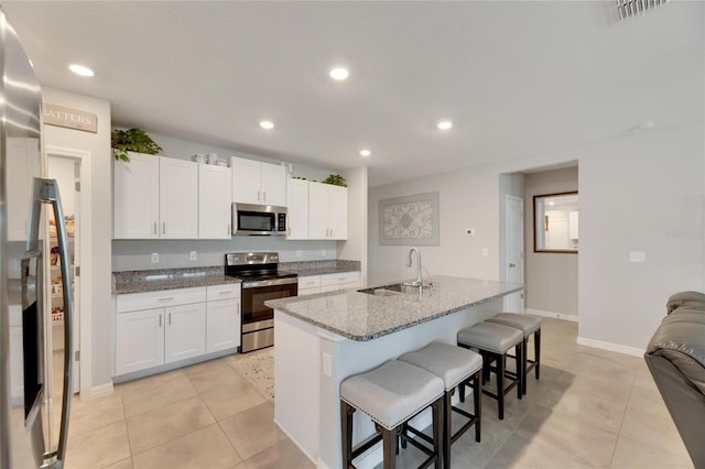 kitchen featuring appliances with stainless steel finishes, light stone counters, sink, a center island with sink, and white cabinets