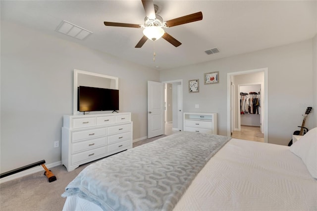 bedroom featuring a spacious closet, a closet, ceiling fan, and light colored carpet