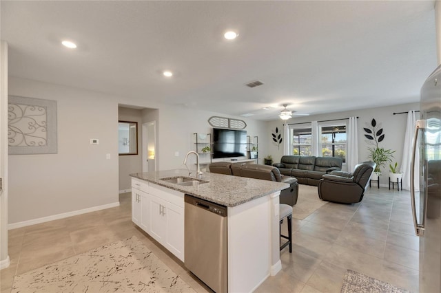 kitchen with appliances with stainless steel finishes, light stone counters, a kitchen island with sink, sink, and white cabinetry