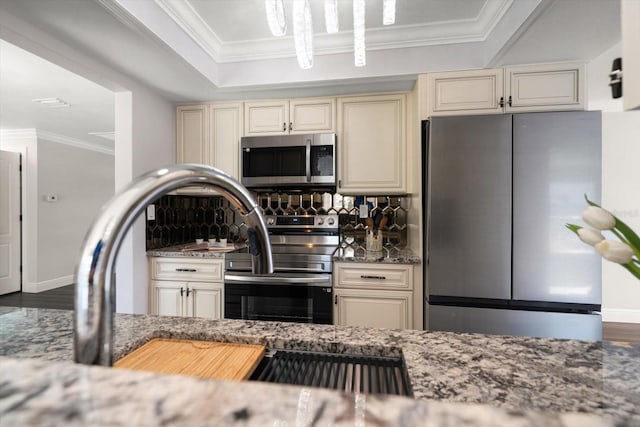 kitchen with cream cabinetry, light stone counters, backsplash, and appliances with stainless steel finishes