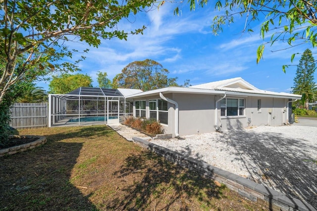 rear view of house with a fenced in pool, glass enclosure, and a lawn