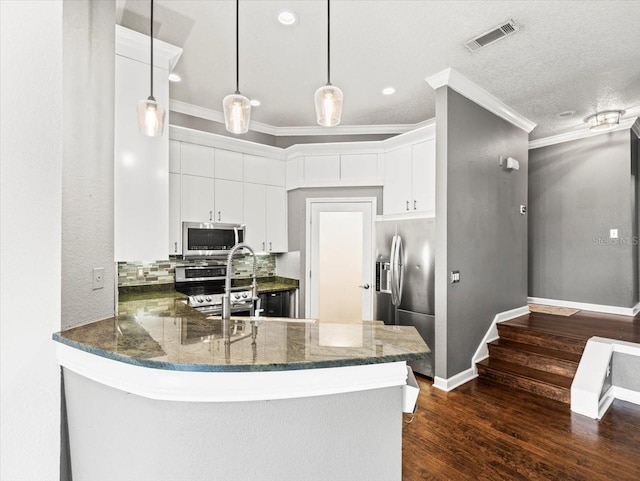 kitchen with kitchen peninsula, appliances with stainless steel finishes, white cabinets, and hanging light fixtures