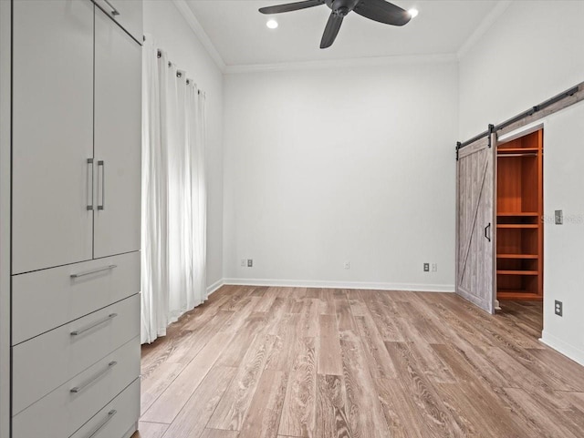 unfurnished bedroom with a barn door, light hardwood / wood-style flooring, ceiling fan, and crown molding