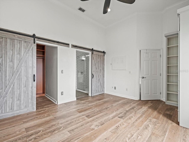 unfurnished bedroom featuring light wood-type flooring, a barn door, ensuite bathroom, and ceiling fan