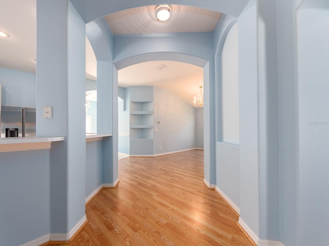 hall featuring built in shelves, light hardwood / wood-style floors, and an inviting chandelier