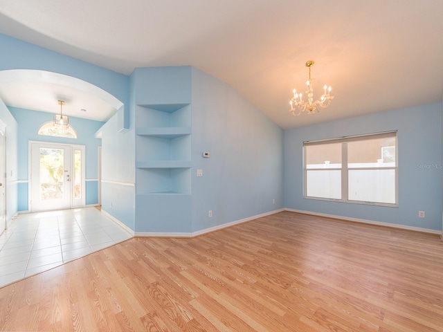 unfurnished living room featuring built in shelves, light wood-type flooring, an inviting chandelier, and french doors