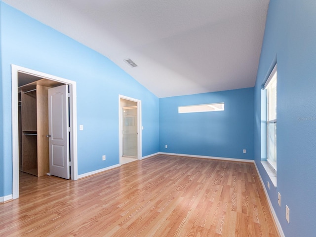 unfurnished bedroom featuring ensuite bath, a spacious closet, light hardwood / wood-style flooring, and lofted ceiling