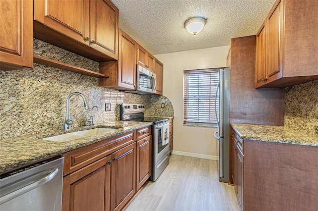 kitchen featuring sink, light stone counters, light hardwood / wood-style floors, decorative backsplash, and appliances with stainless steel finishes