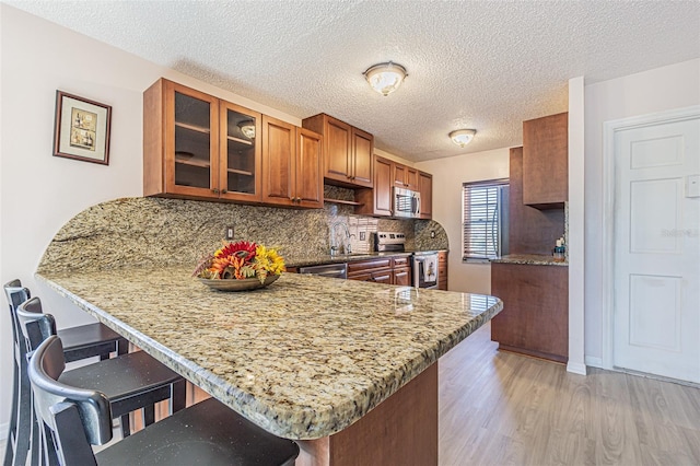 kitchen with a breakfast bar area, light wood-type flooring, light stone counters, kitchen peninsula, and stainless steel appliances