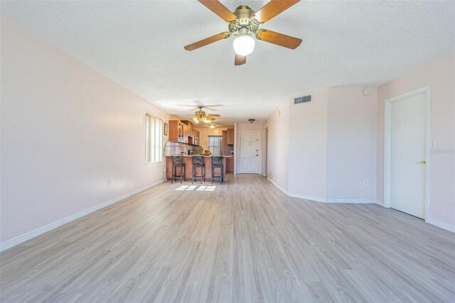 unfurnished living room with ceiling fan, light hardwood / wood-style floors, and a textured ceiling