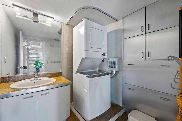 washroom featuring a textured ceiling, sink, stacked washing maching and dryer, and tile walls