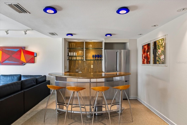 bar with stainless steel fridge and a textured ceiling