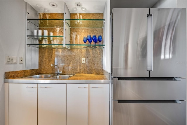 bar with stainless steel refrigerator, white cabinetry, sink, and decorative backsplash