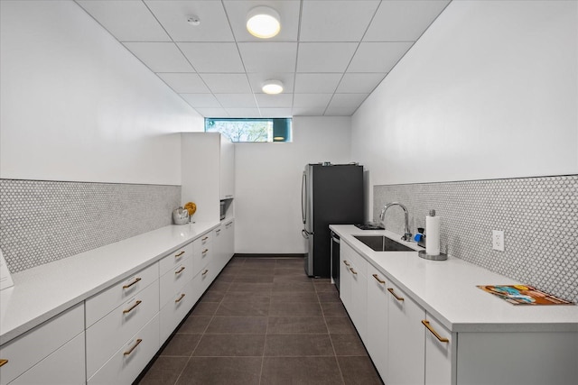 kitchen featuring stainless steel fridge, a drop ceiling, dark tile patterned floors, sink, and white cabinets