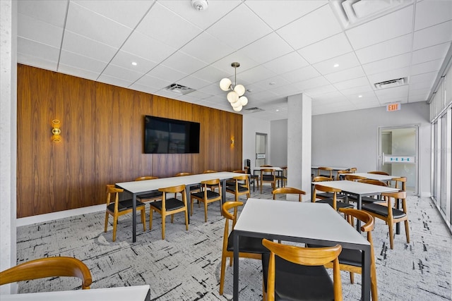 carpeted dining space with a paneled ceiling and wooden walls