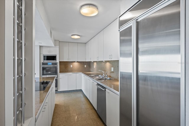kitchen with tile patterned floors, a sink, tasteful backsplash, built in appliances, and white cabinetry