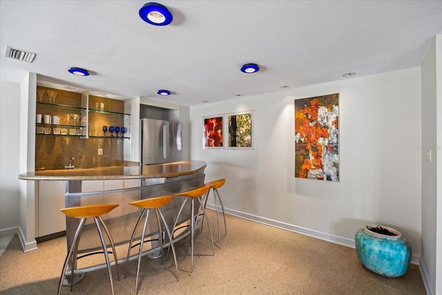 bar featuring light speckled floor, visible vents, baseboards, freestanding refrigerator, and bar