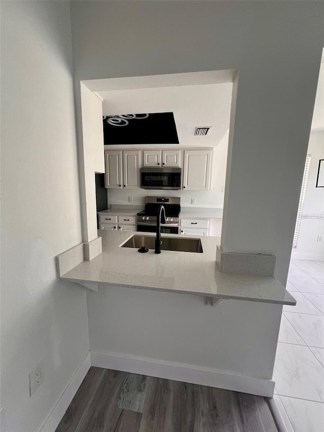 kitchen with appliances with stainless steel finishes, light stone counters, sink, white cabinets, and dark hardwood / wood-style floors