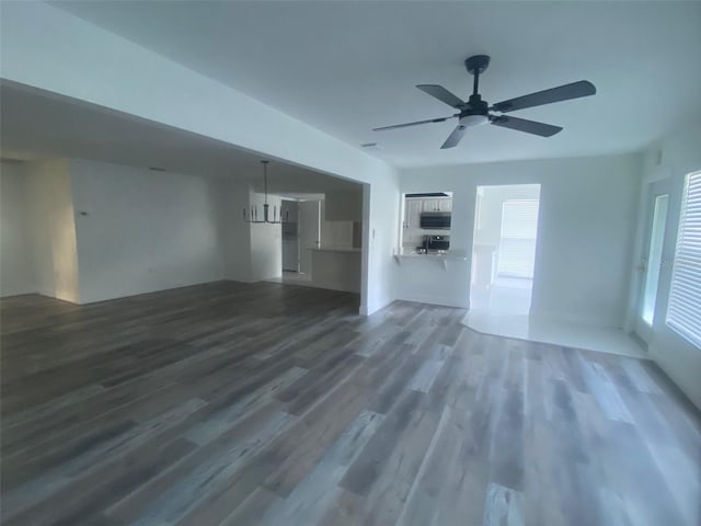 unfurnished living room with a wealth of natural light, dark hardwood / wood-style flooring, and ceiling fan with notable chandelier