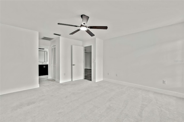 unfurnished bedroom with ceiling fan, light colored carpet, a closet, and ensuite bath