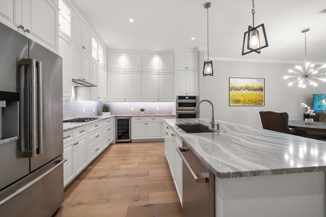 kitchen with appliances with stainless steel finishes, white cabinetry, beverage cooler, and a kitchen island with sink