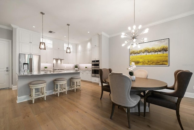 dining room featuring an inviting chandelier, ornamental molding, sink, and light hardwood / wood-style flooring