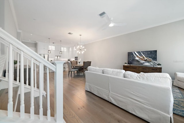 living room with ceiling fan with notable chandelier, wood-type flooring, and crown molding