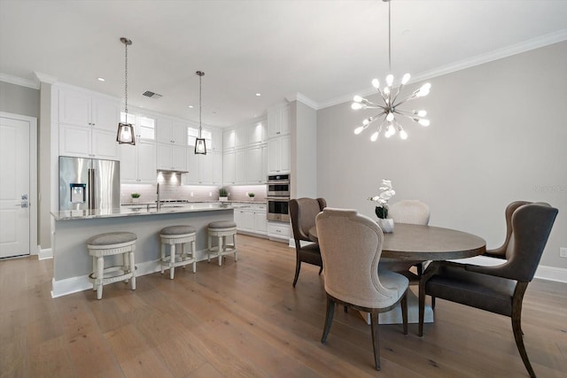 dining space with sink, light hardwood / wood-style flooring, an inviting chandelier, and ornamental molding