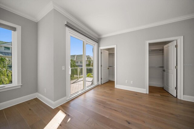 unfurnished bedroom with hardwood / wood-style floors, a closet, a spacious closet, and multiple windows