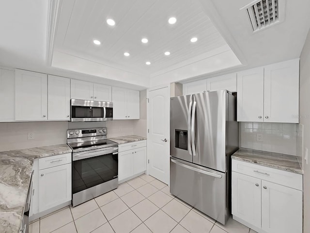 kitchen with a tray ceiling, white cabinetry, stainless steel appliances, and light stone counters