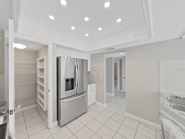 kitchen with white cabinetry, light stone countertops, a raised ceiling, stainless steel fridge with ice dispenser, and light tile patterned floors