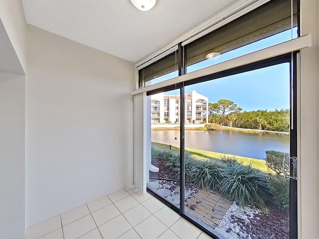 doorway to outside with plenty of natural light, light tile patterned flooring, a water view, and a textured ceiling