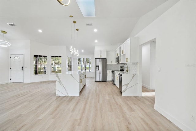 kitchen featuring white cabinets, decorative light fixtures, light hardwood / wood-style floors, light stone counters, and stainless steel appliances