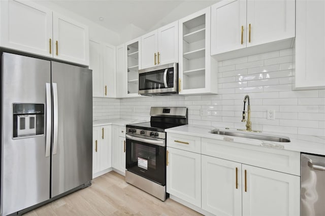 kitchen featuring sink, light stone counters, light hardwood / wood-style floors, white cabinets, and appliances with stainless steel finishes