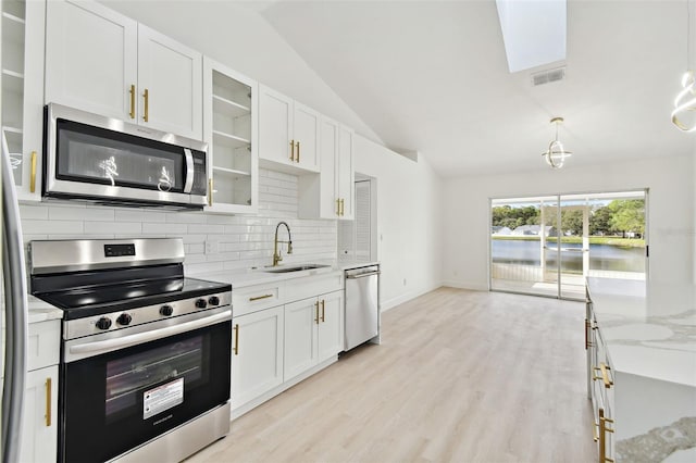 kitchen with light stone counters, stainless steel appliances, lofted ceiling with skylight, sink, and white cabinets