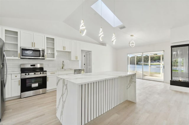 kitchen featuring white cabinetry, light stone counters, decorative light fixtures, vaulted ceiling with skylight, and appliances with stainless steel finishes