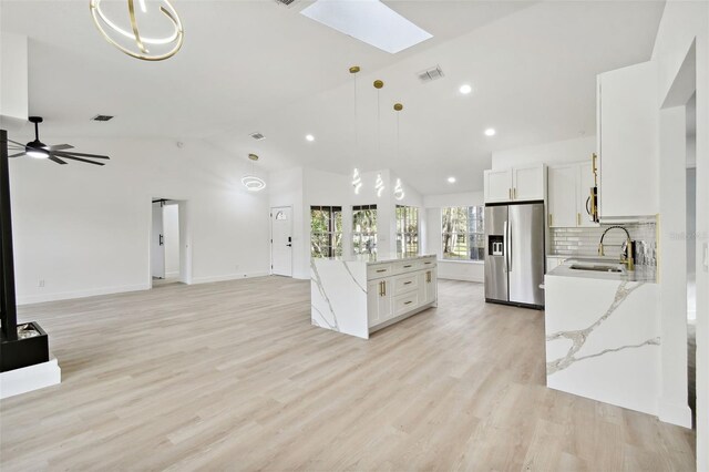 kitchen with white cabinetry, hanging light fixtures, stainless steel appliances, light hardwood / wood-style floors, and vaulted ceiling with skylight