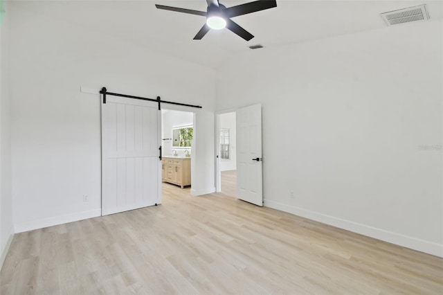 unfurnished bedroom featuring lofted ceiling, ceiling fan, a barn door, light wood-type flooring, and connected bathroom