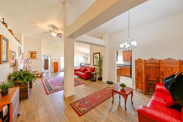 living room with ceiling fan with notable chandelier, a high ceiling, and light wood-type flooring