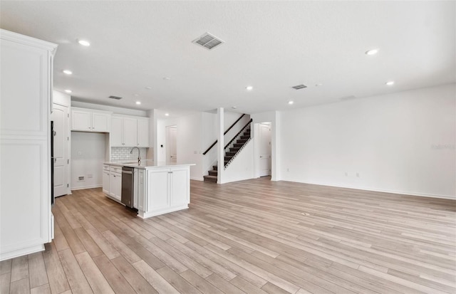 kitchen with light wood-type flooring, tasteful backsplash, stainless steel dishwasher, white cabinetry, and an island with sink