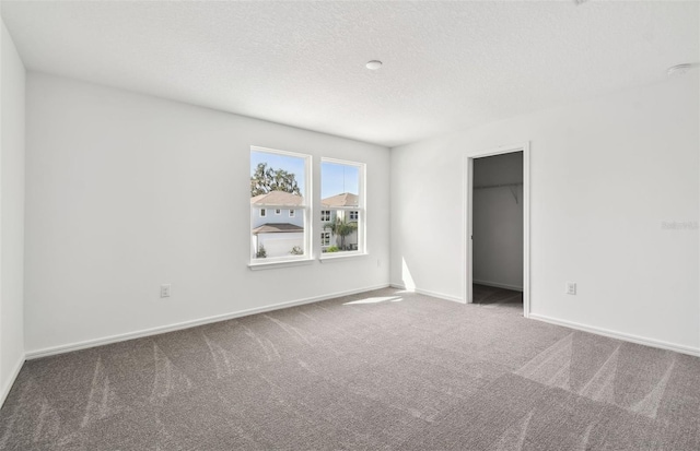 unfurnished bedroom with carpet flooring, a spacious closet, a closet, and a textured ceiling