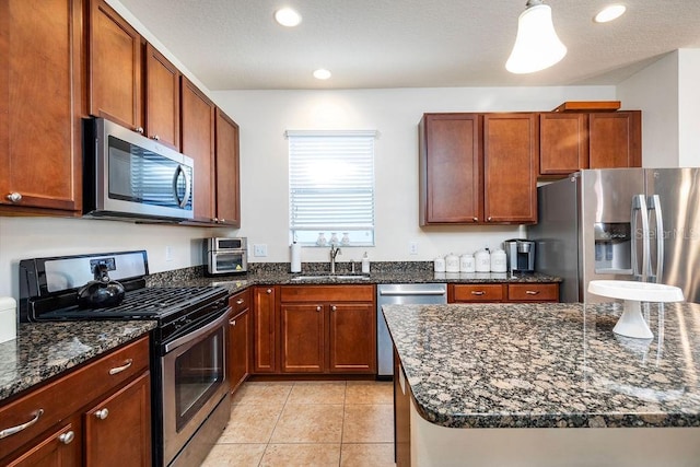 kitchen featuring sink, hanging light fixtures, stainless steel appliances, dark stone countertops, and light tile patterned floors