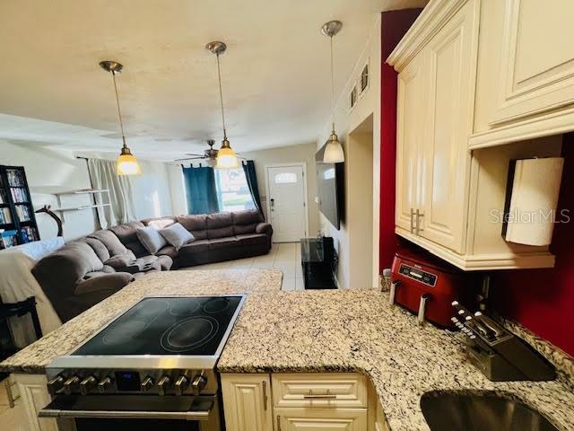 kitchen with light stone countertops, stainless steel range, ceiling fan, pendant lighting, and cream cabinetry