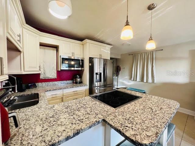 kitchen with kitchen peninsula, appliances with stainless steel finishes, sink, light tile patterned floors, and decorative light fixtures