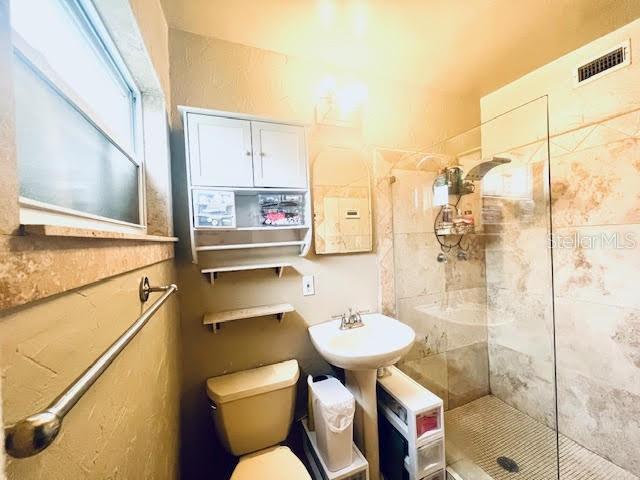 bathroom with a tile shower, toilet, and sink