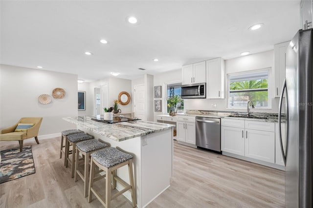 kitchen with light wood-style flooring, a kitchen island, a breakfast bar area, light stone countertops, and stainless steel appliances